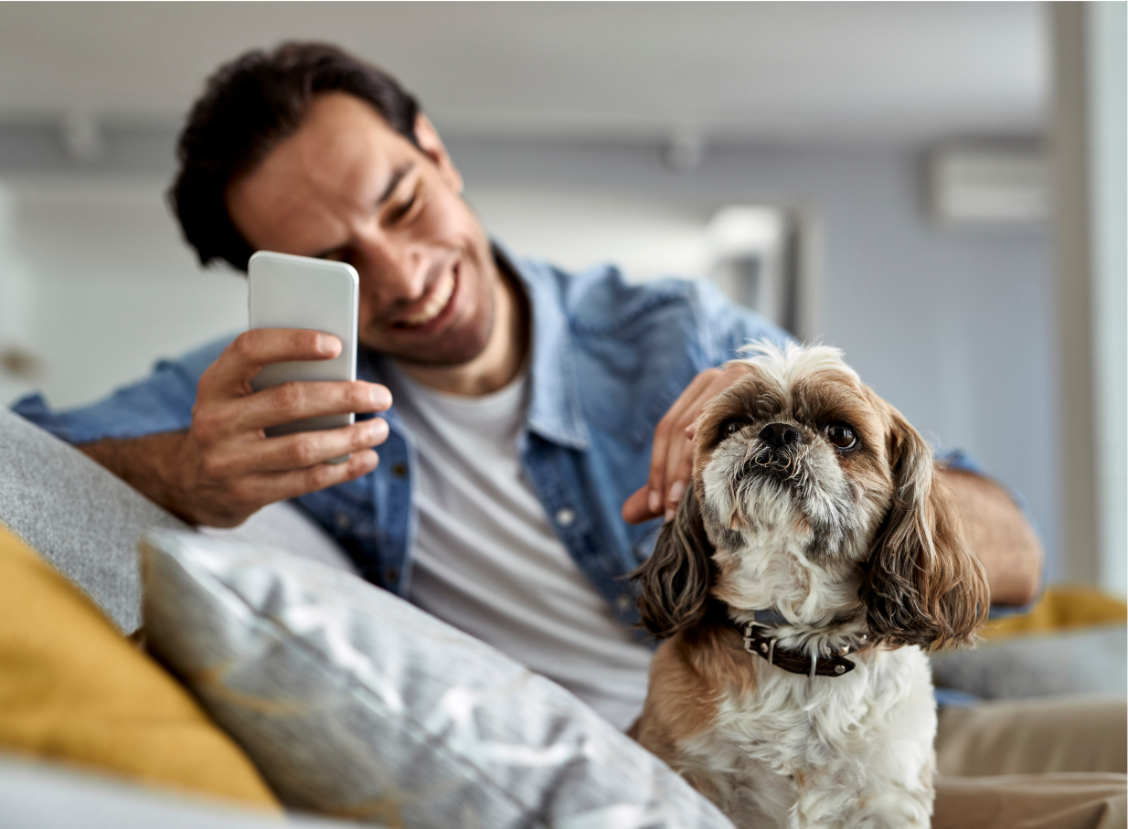 Man petting small dog while holding a phone and relaxing on a couch