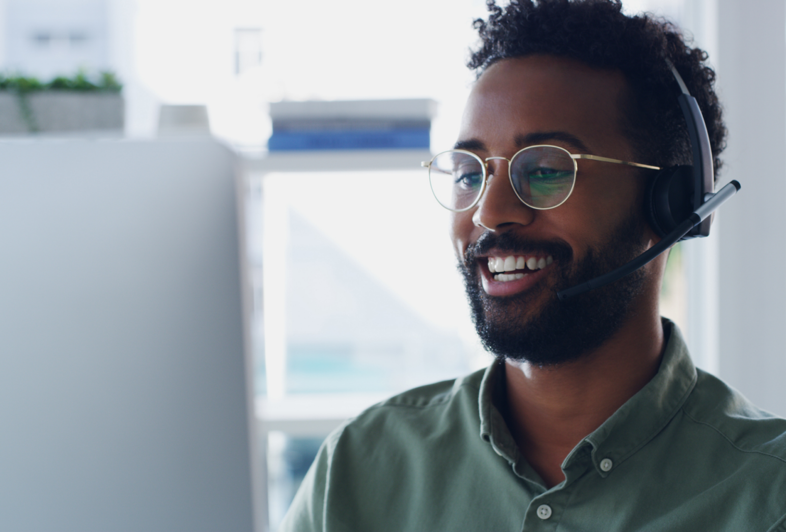 A smiling young man looking at a computer screen and wearing a headset