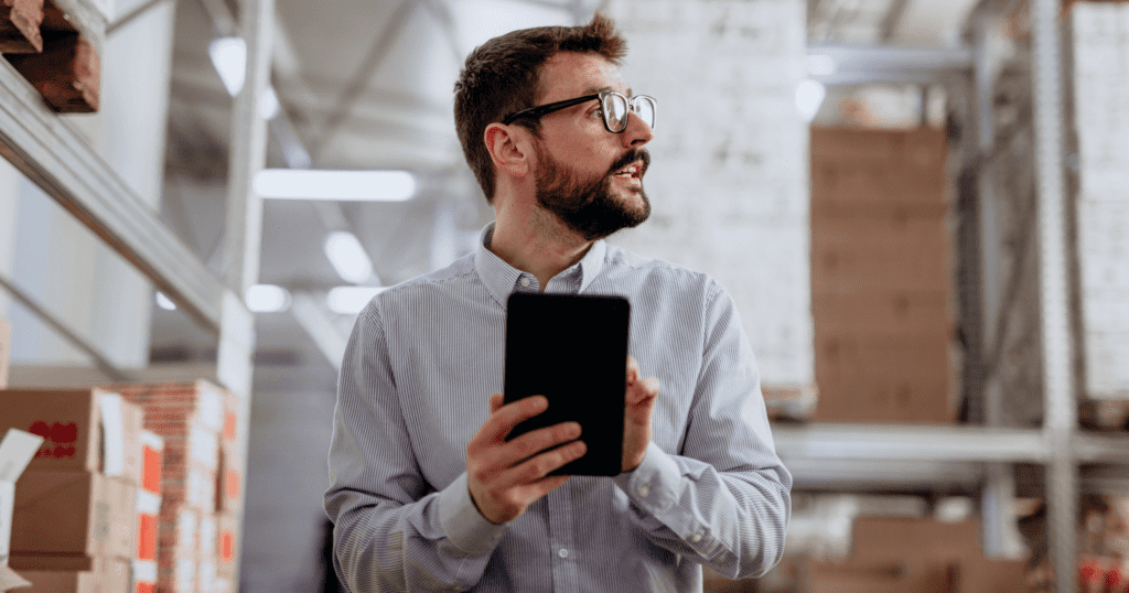 A worker in a warehouse looking up attentively while using a mini tablet.