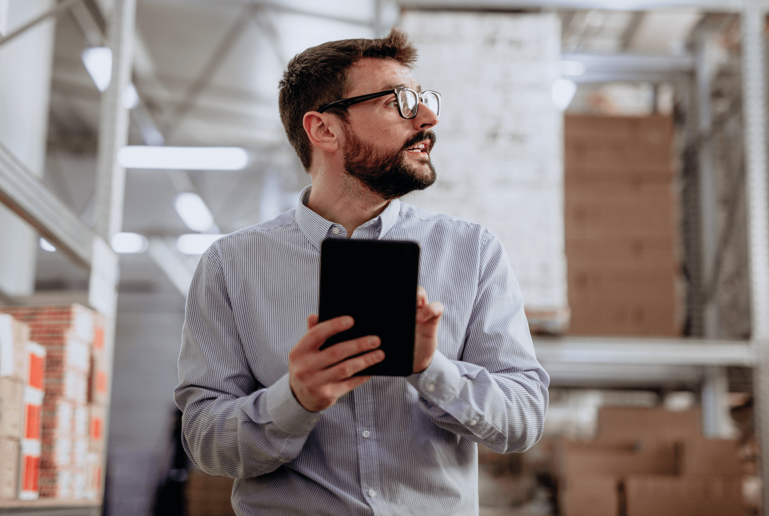 A worker in a warehouse looking up attentively while using a mini tablet.