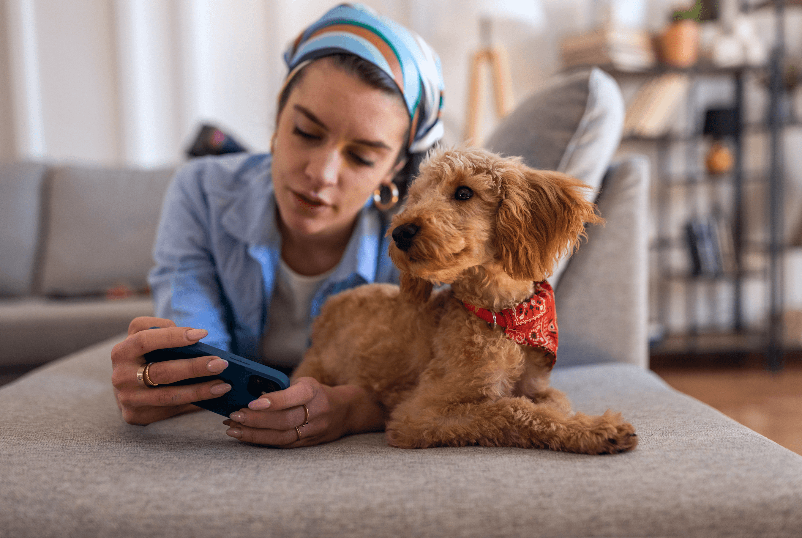 A young woman lying on her stomach using her mobile phone, with her dog relaxing next to her.