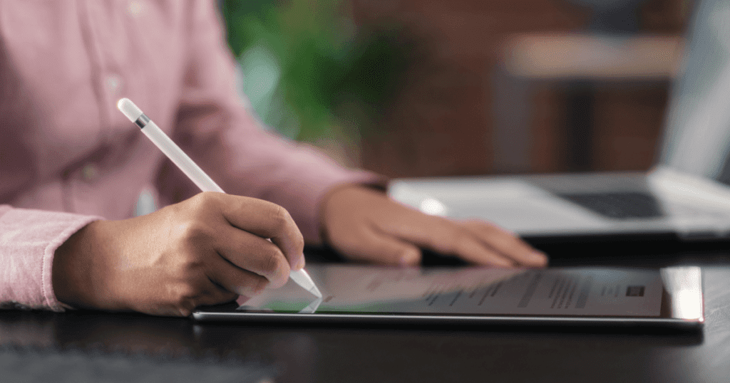 Closeup of a person’s hand writing on a tablet with a stylus