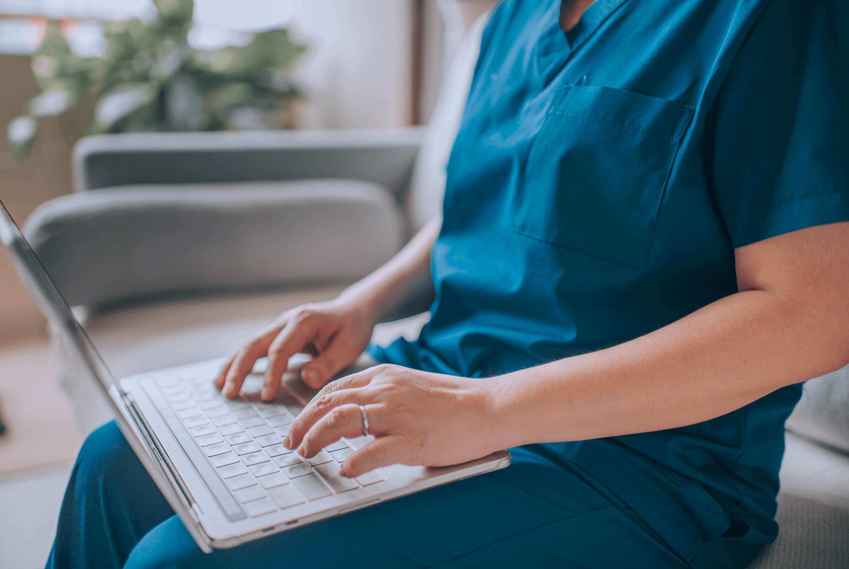 A closeup shot of a vet tech using a laptop, sitting on a couch.