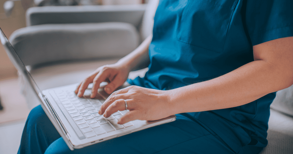 A closeup shot of a vet tech using a laptop, sitting on a couch.