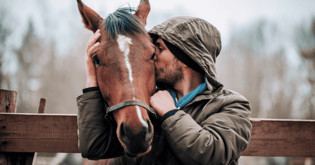 A man hugging and kissing a horse as it leans over a fence