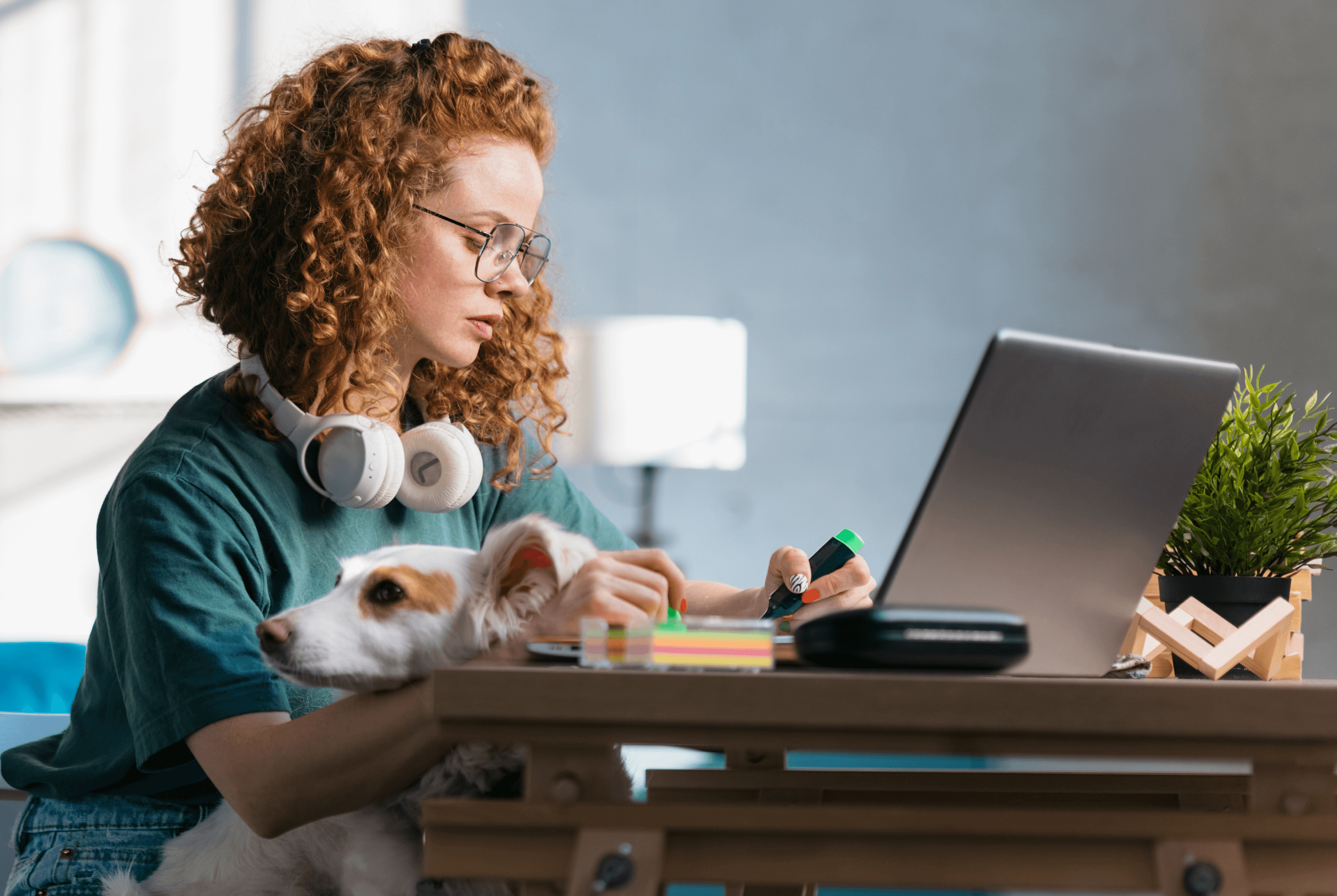 Young woman working on her laptop while her dog rests its chin on her arm.