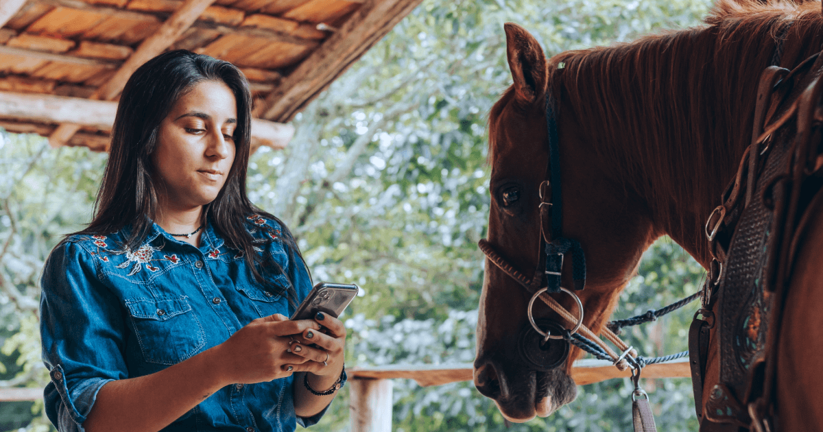 A young woman using a mobile phone next to her horse.