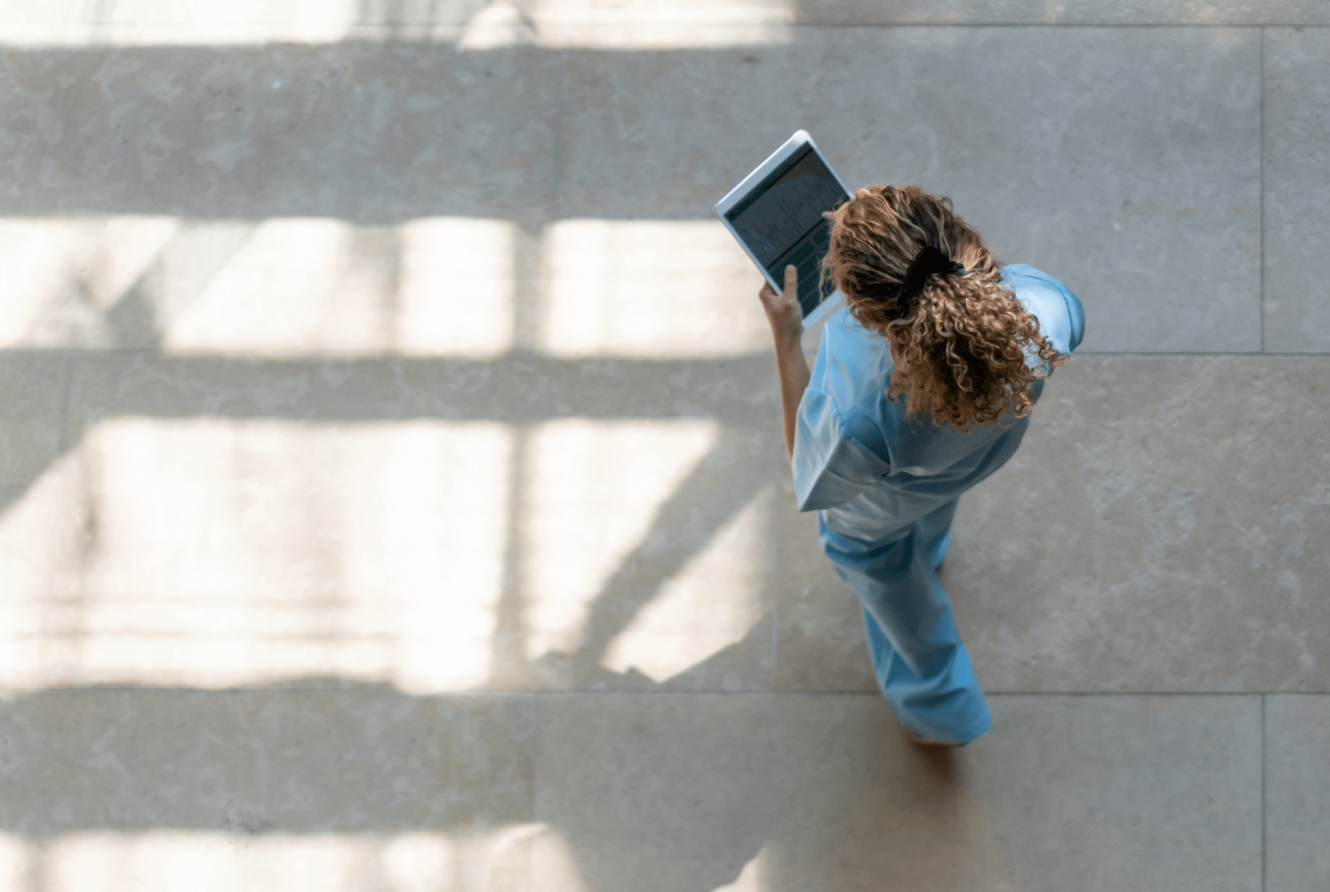 An overhead shot of a vet using a tablet while walking across a brightly lit stone floor.