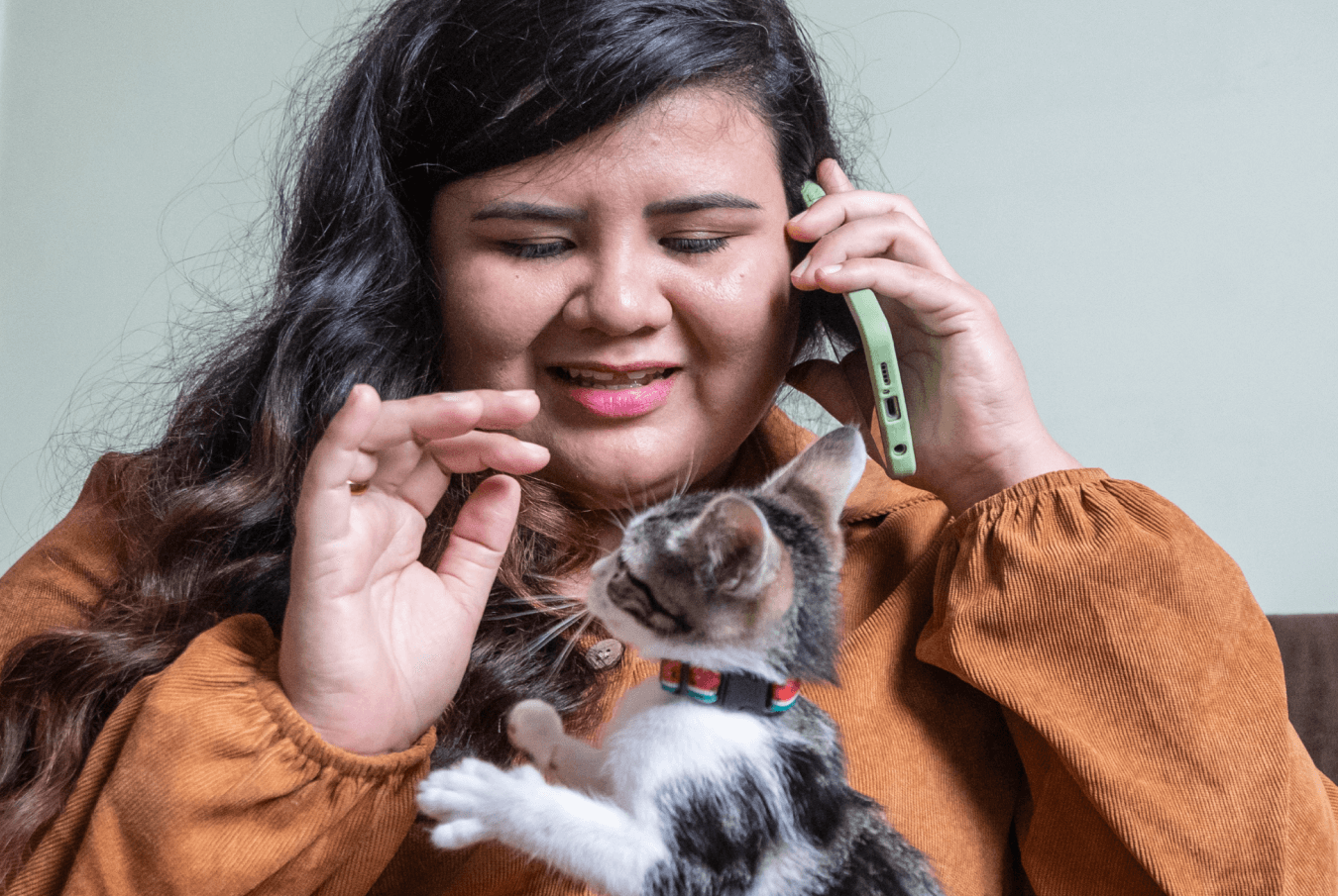 Young pet owner on the phone playing with a kitten