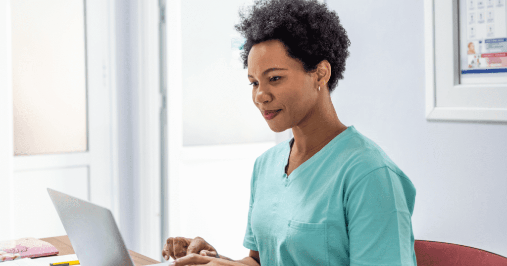 Female vet wearing teal scrubs typing on her laptop in the office