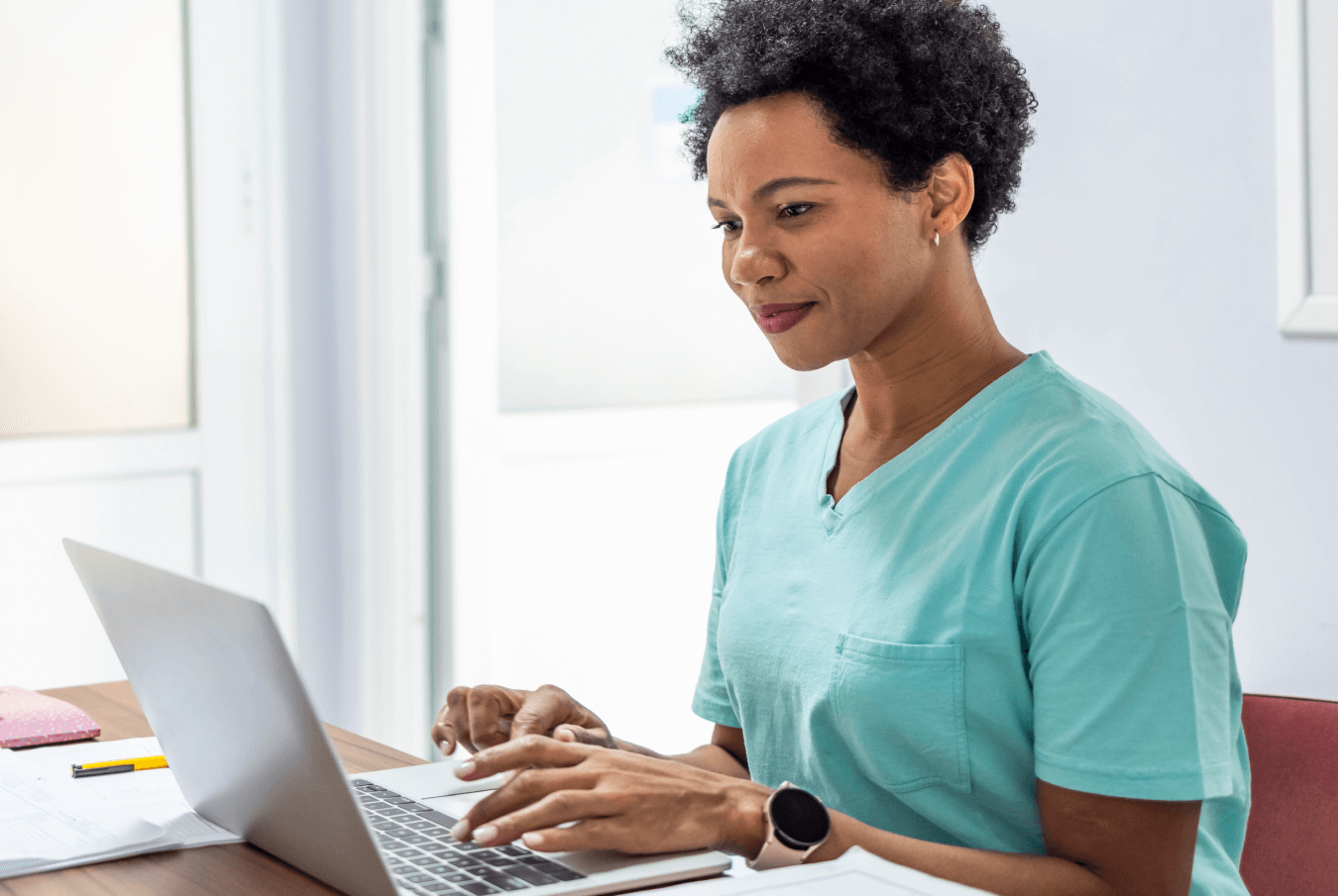 Female vet wearing teal scrubs typing on her laptop in the office