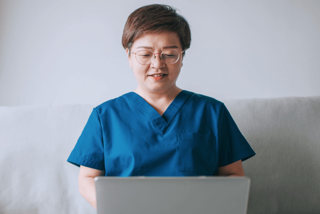 Female vet wearing glasses typing into her laptop sitting on a white couch