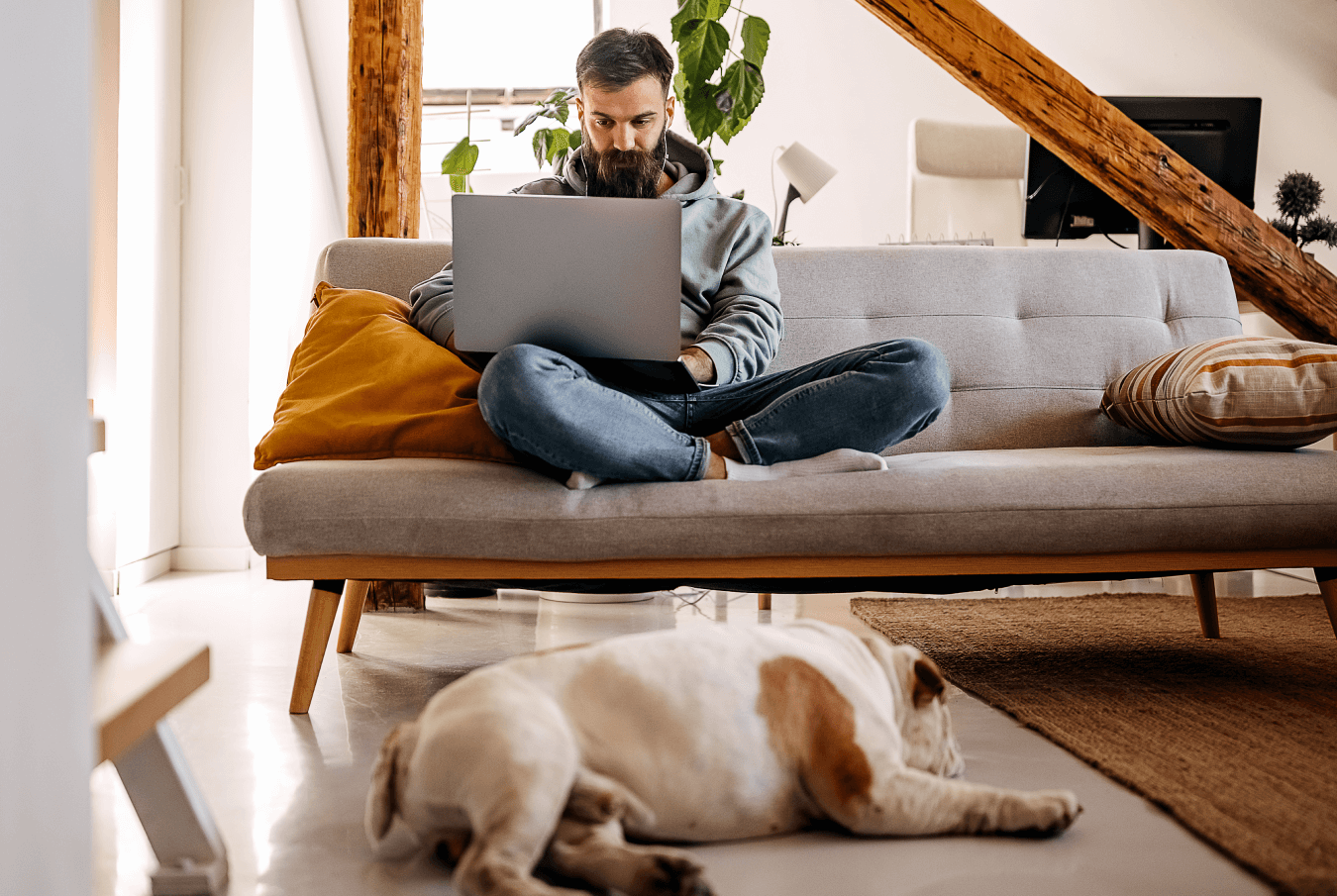 Pet owner sitting cross-legged on a couch with a bulldog laying on the floor at his feet.