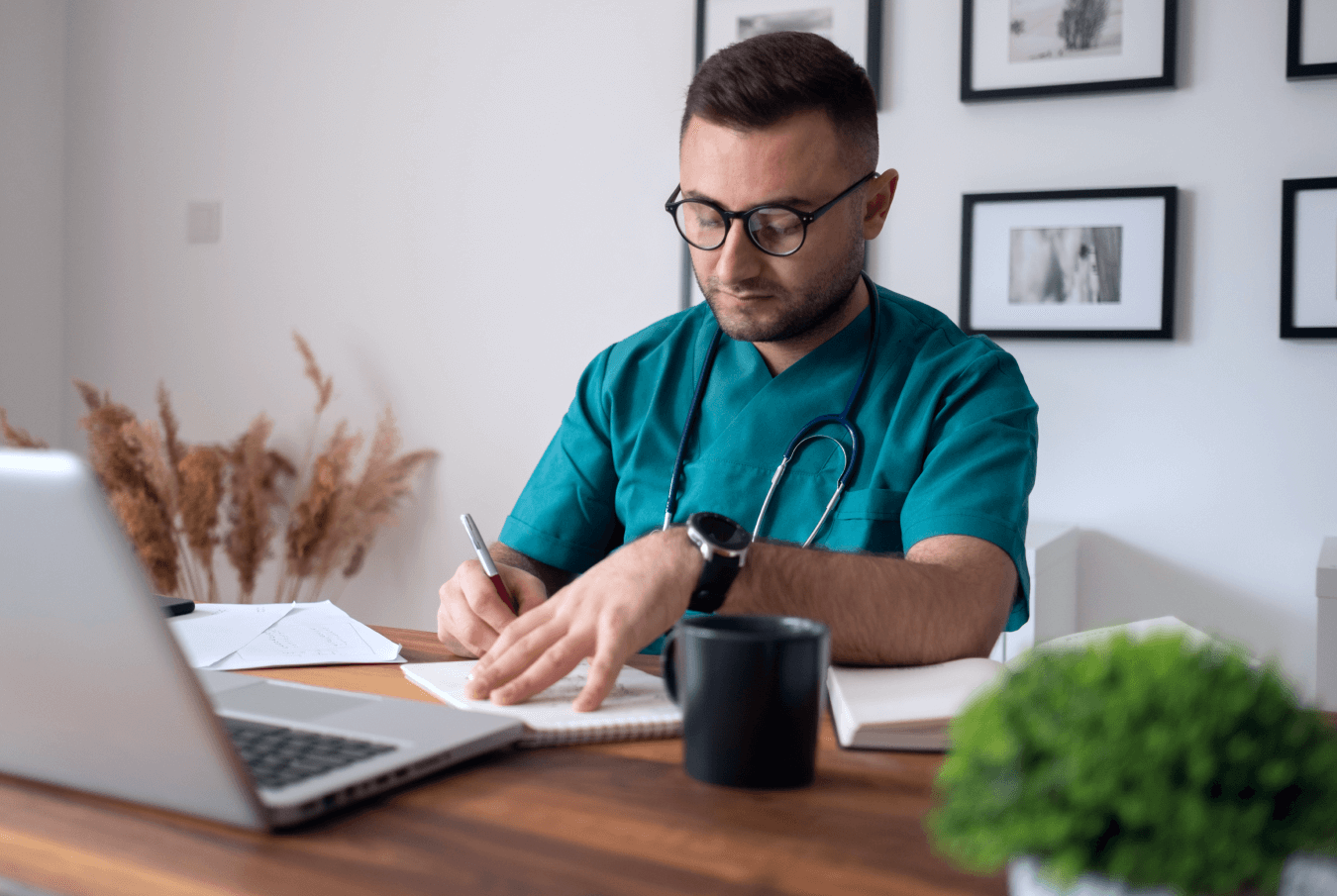 Vet writing thoughtfully in his office at his desk with an open laptop