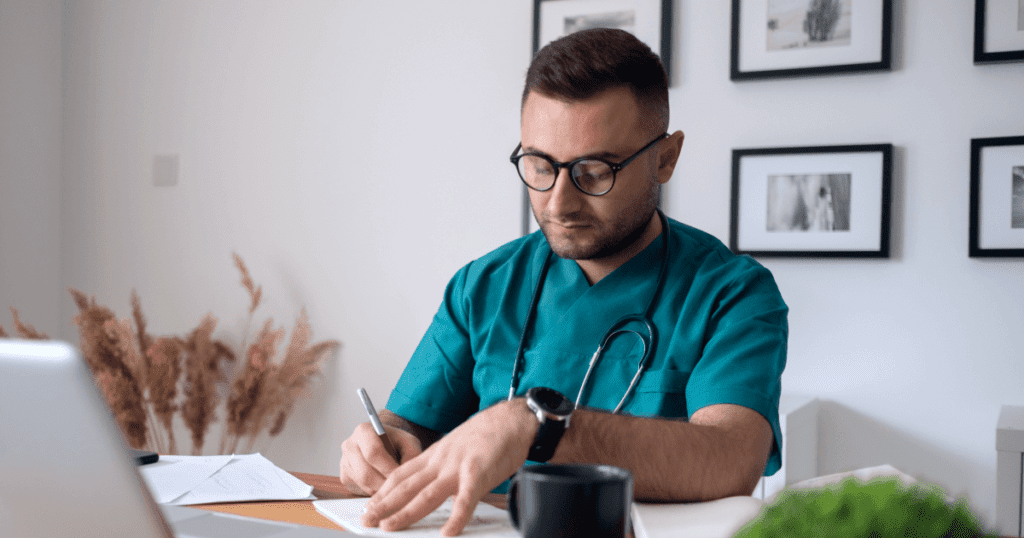 Vet writing thoughtfully in his office at his desk with an open laptop