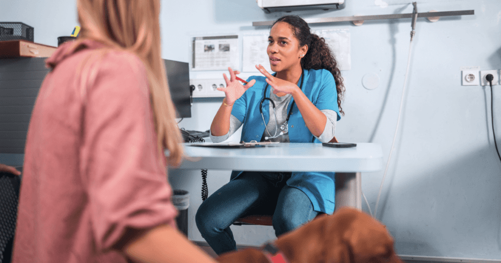 Vet sitting across from a pet owner whie her dog sits next to her, talking animatedly