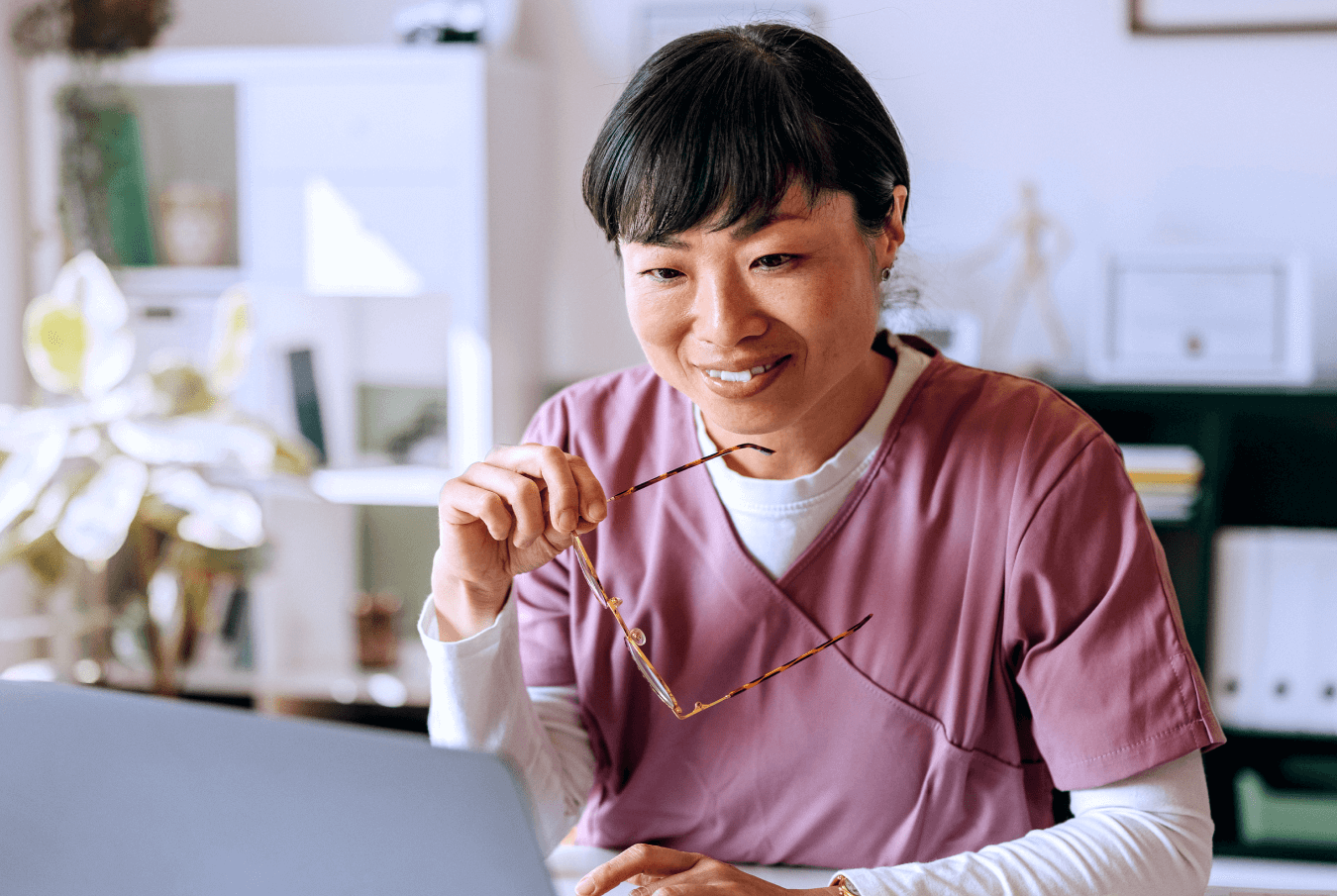 Smiling vet removing glasses while looking at data on her laptop screen