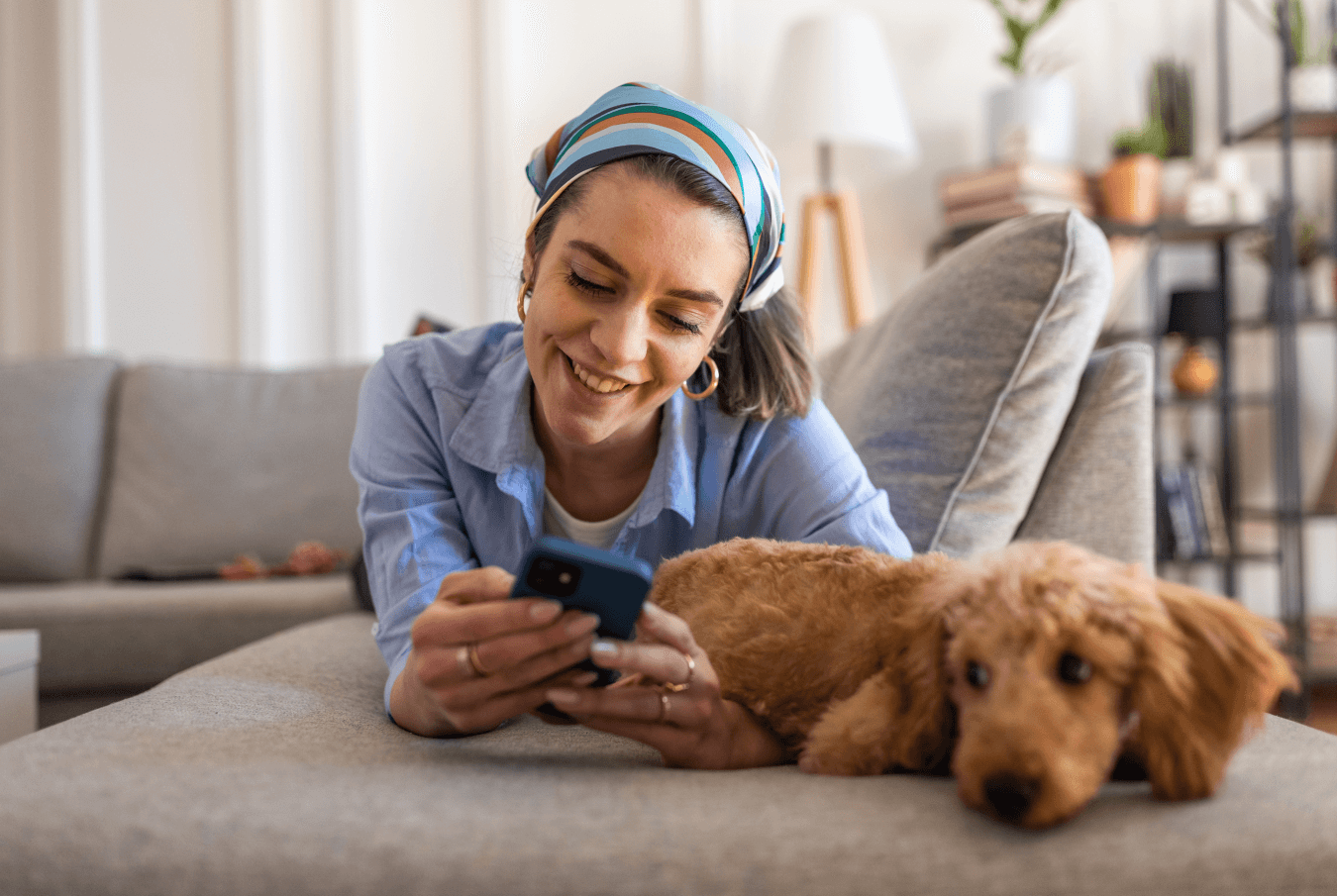 Woman laying on a couch with her poodle checking her phone