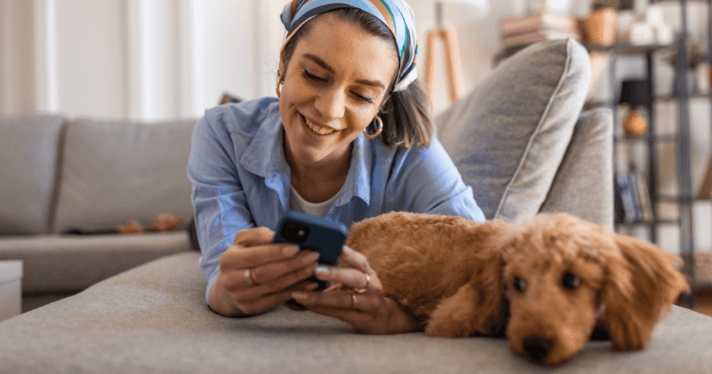 Woman laying on a couch with her poodle checking her phone