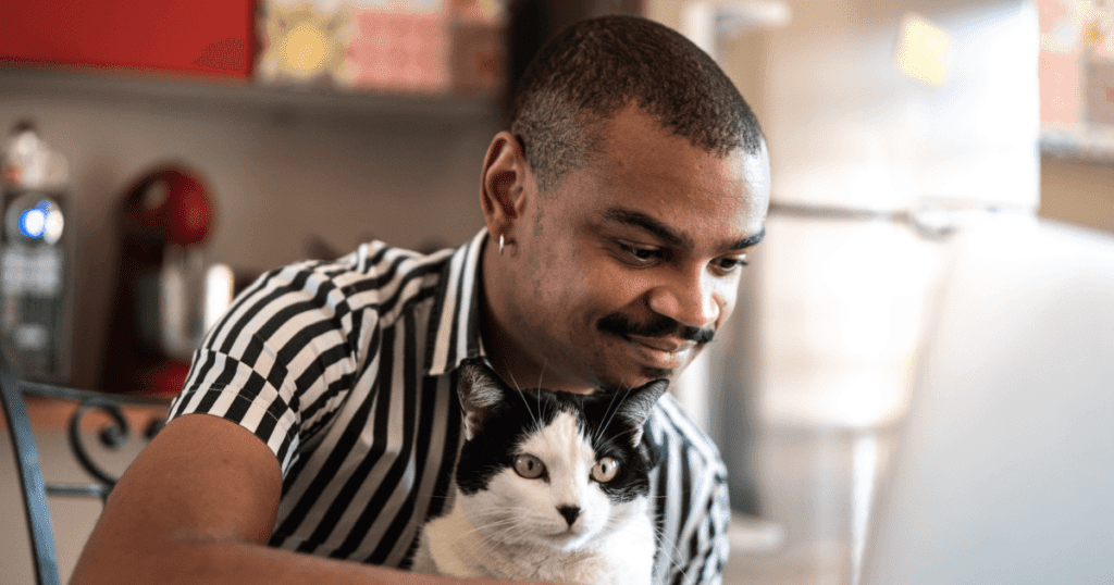 Smiling pet owner using his laptop in a kitchen area with his cat on his lap