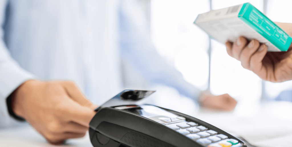 A customer paying for veterinary medication with a credit card tap, with the person handing them the medication in the foreground