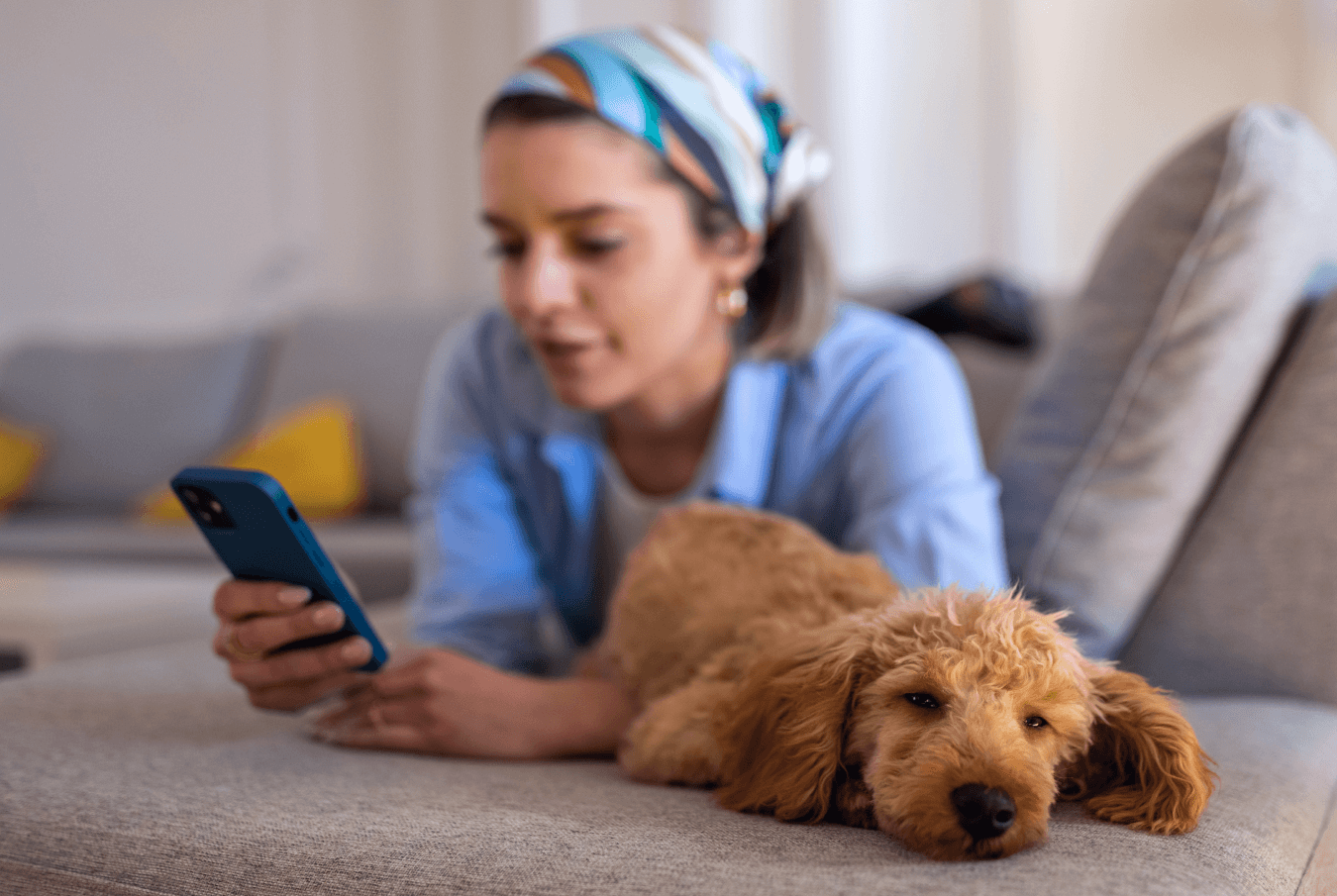 Young woman lying on the couch with a sleepy poodle looking at her phone