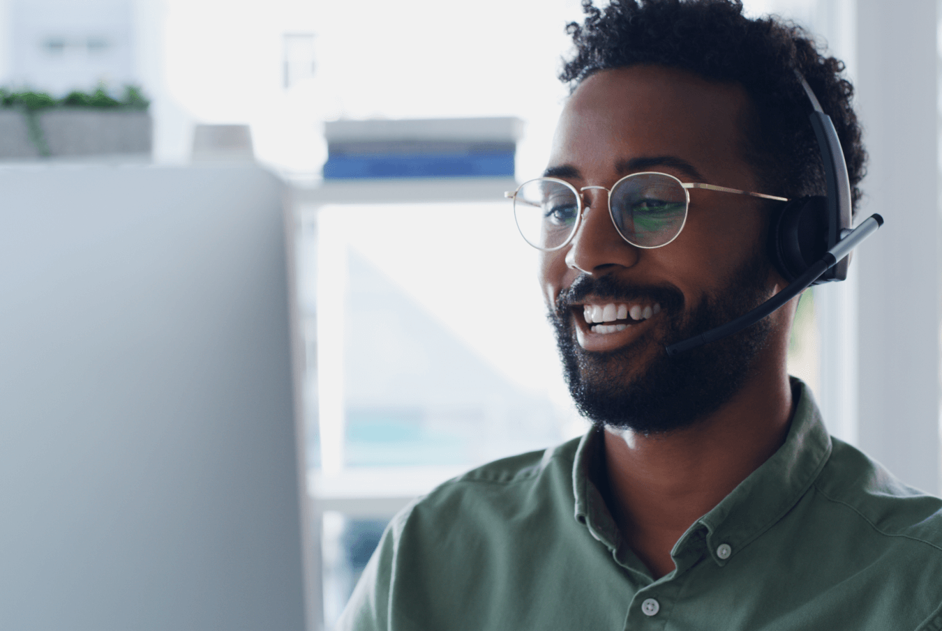 Smiling tech support person looking at his desktop monitor screen and talking using a headset