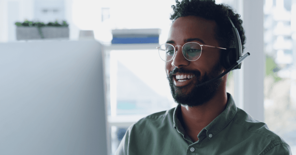 Smiling tech support person looking at his desktop monitor screen and talking using a headset