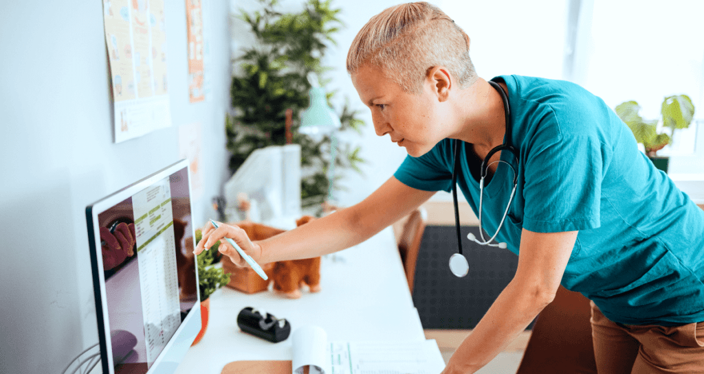 Woman vet standing in front of a desktop computer entering data into a touch screen monitor